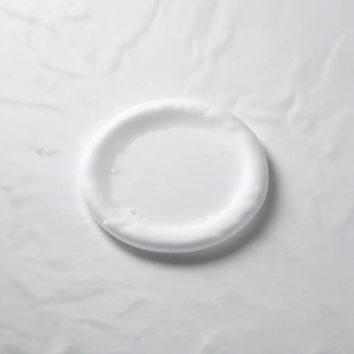 Un dischetto di cotone bianco imbevuto di un liquido trasparente su sfondo neutro